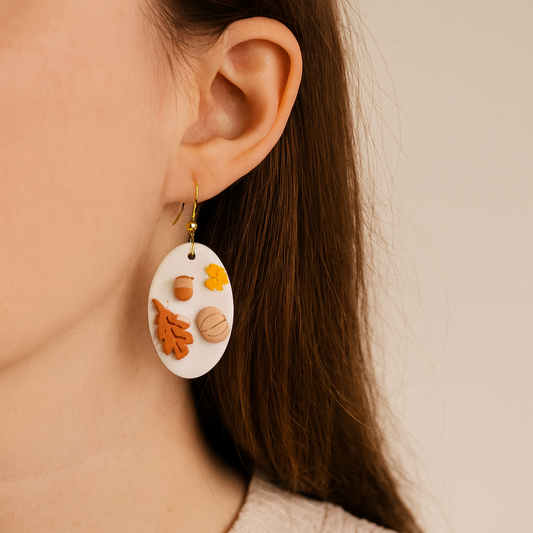 Close-up of a person wearing a pair of earrings with autumn-themed design.